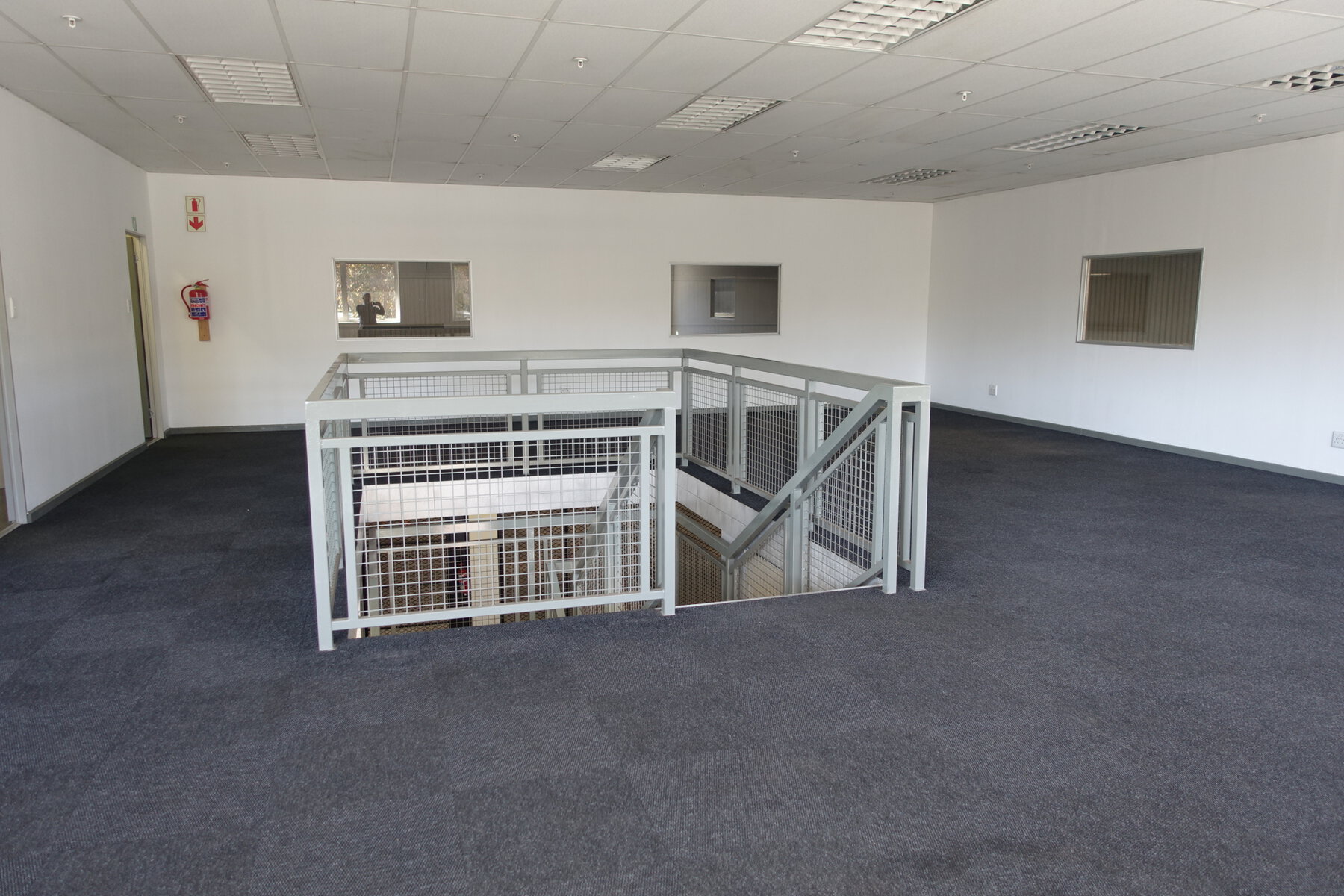 Bright, clean office interior featuring a staircase leading to a lower level, with white walls and large windows providing natural light.