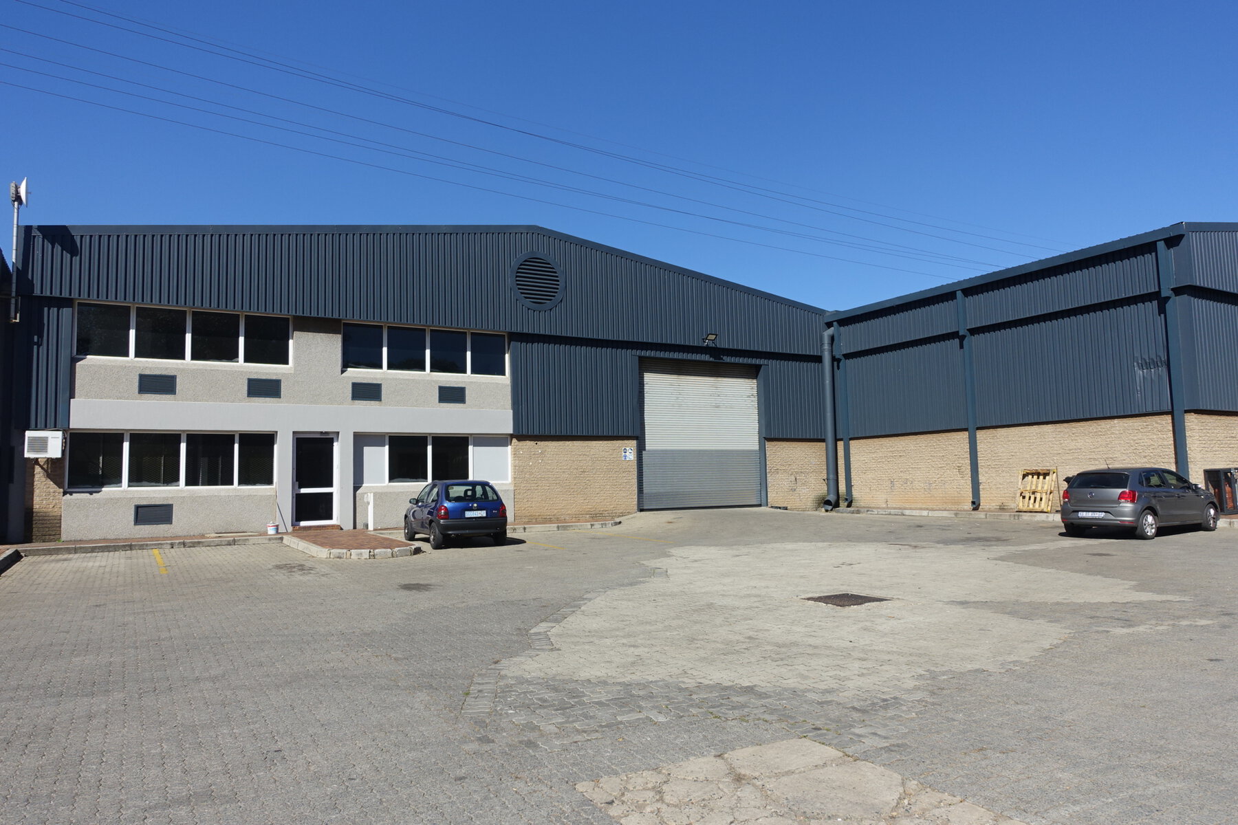 Modern industrial warehouse and office building with large garage doors and parking area, part of Currie Group's facilities established since 1887.
