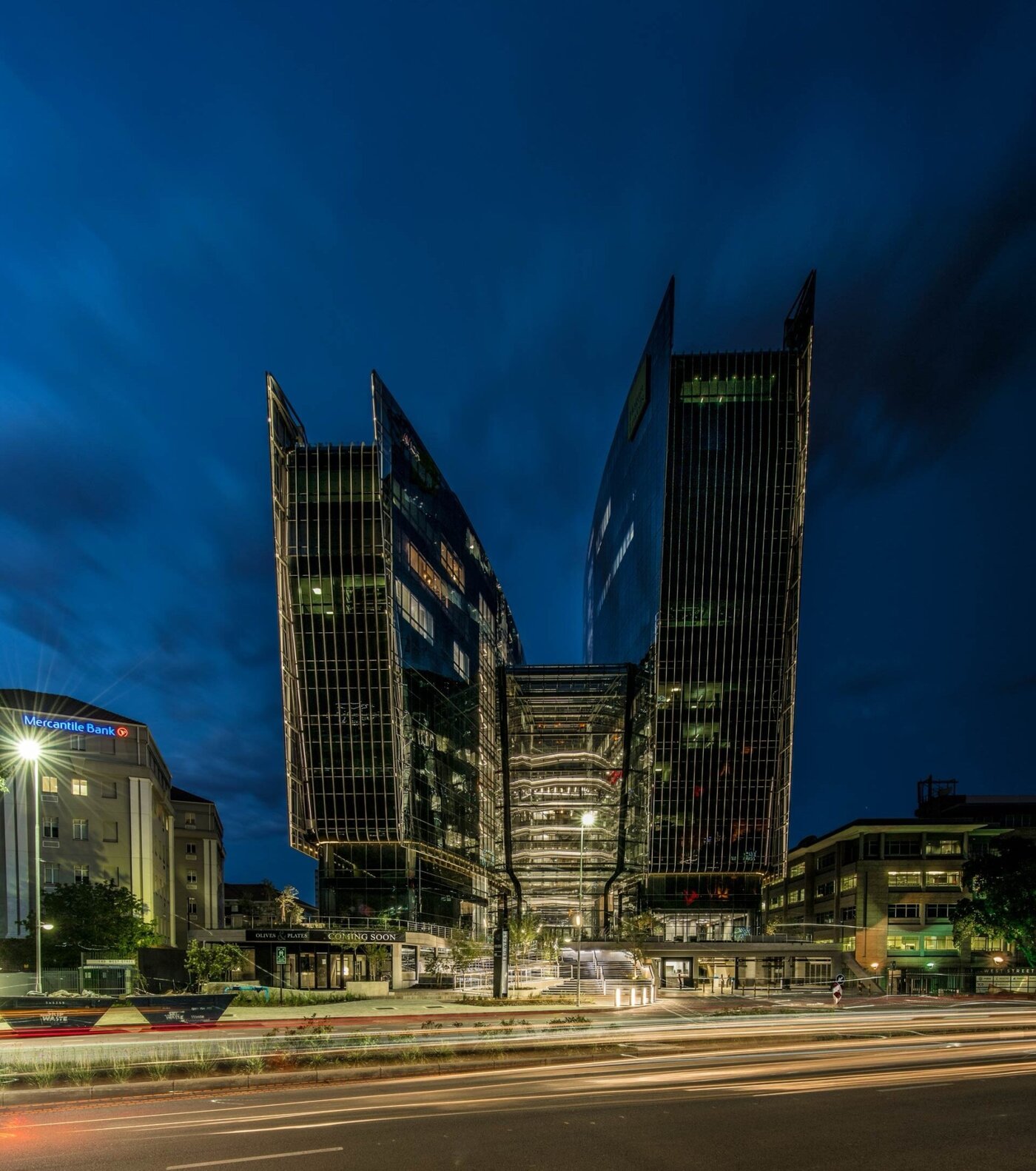 Night view of modern office buildings with glass facades in downtown, illuminated against a dark sky, showcasing contemporary architecture and vibrant city life.