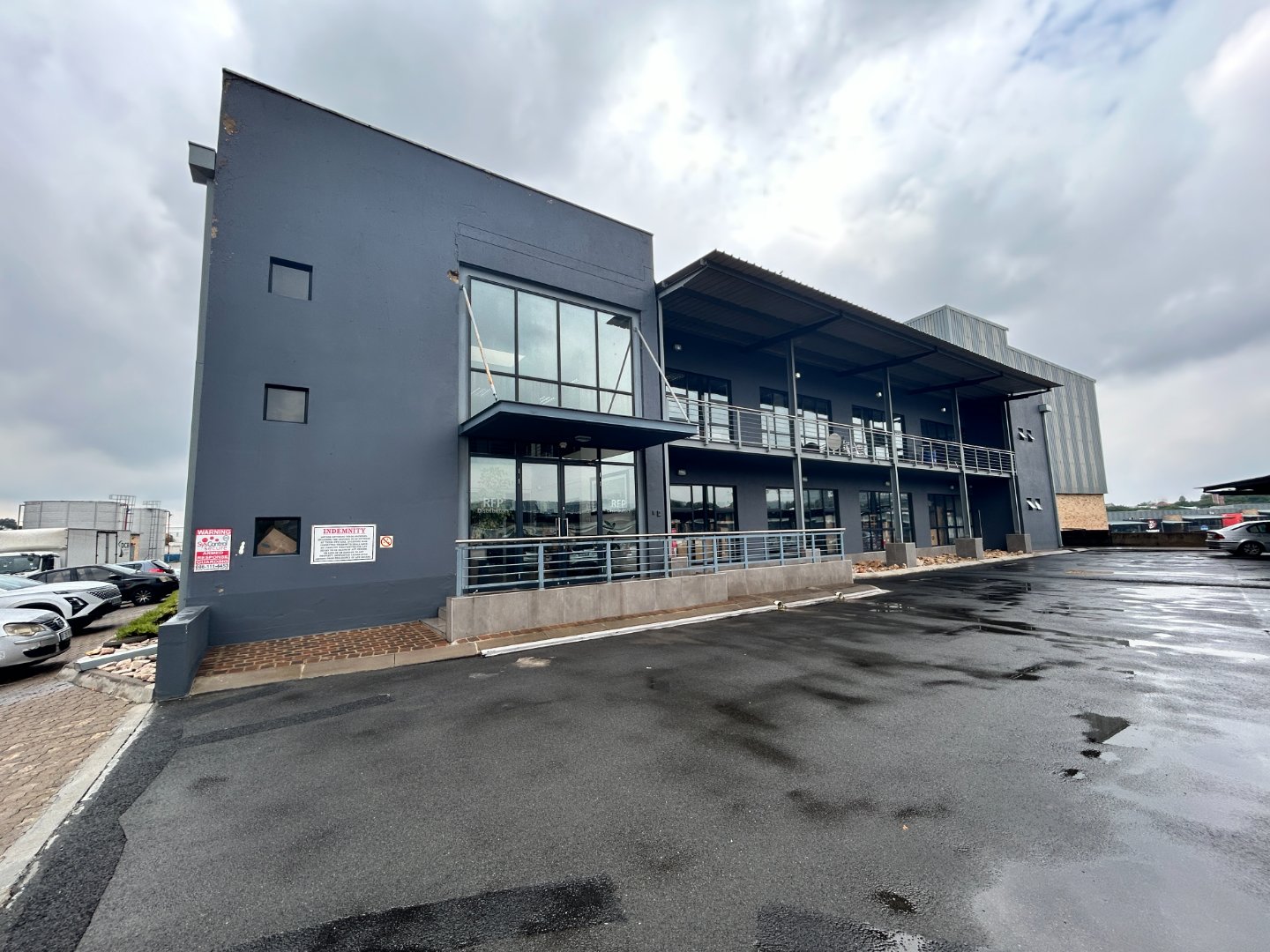 Modern Currie Group office and warehouse building with large glass windows and a sleek dark exterior, situated in an industrial area with a parking lot and overcast sky.