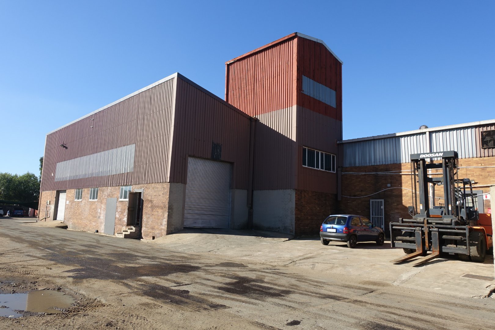 Modern industrial warehouse and office building with a forklift and parked cars, showcasing durable construction and functional design for business operations.