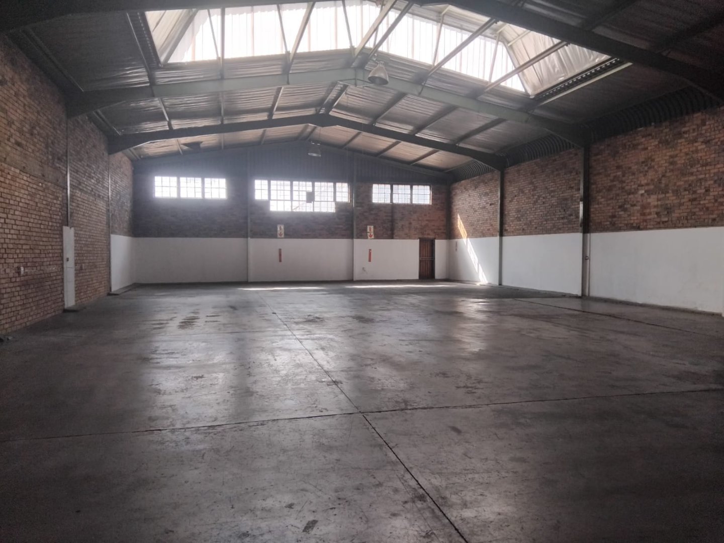 Warehouse interior at Currie Group offices and warehouses. Spacious industrial warehouse with high ceilings, brick walls, and large windows providing natural light, suitable for storage and logistics operations.