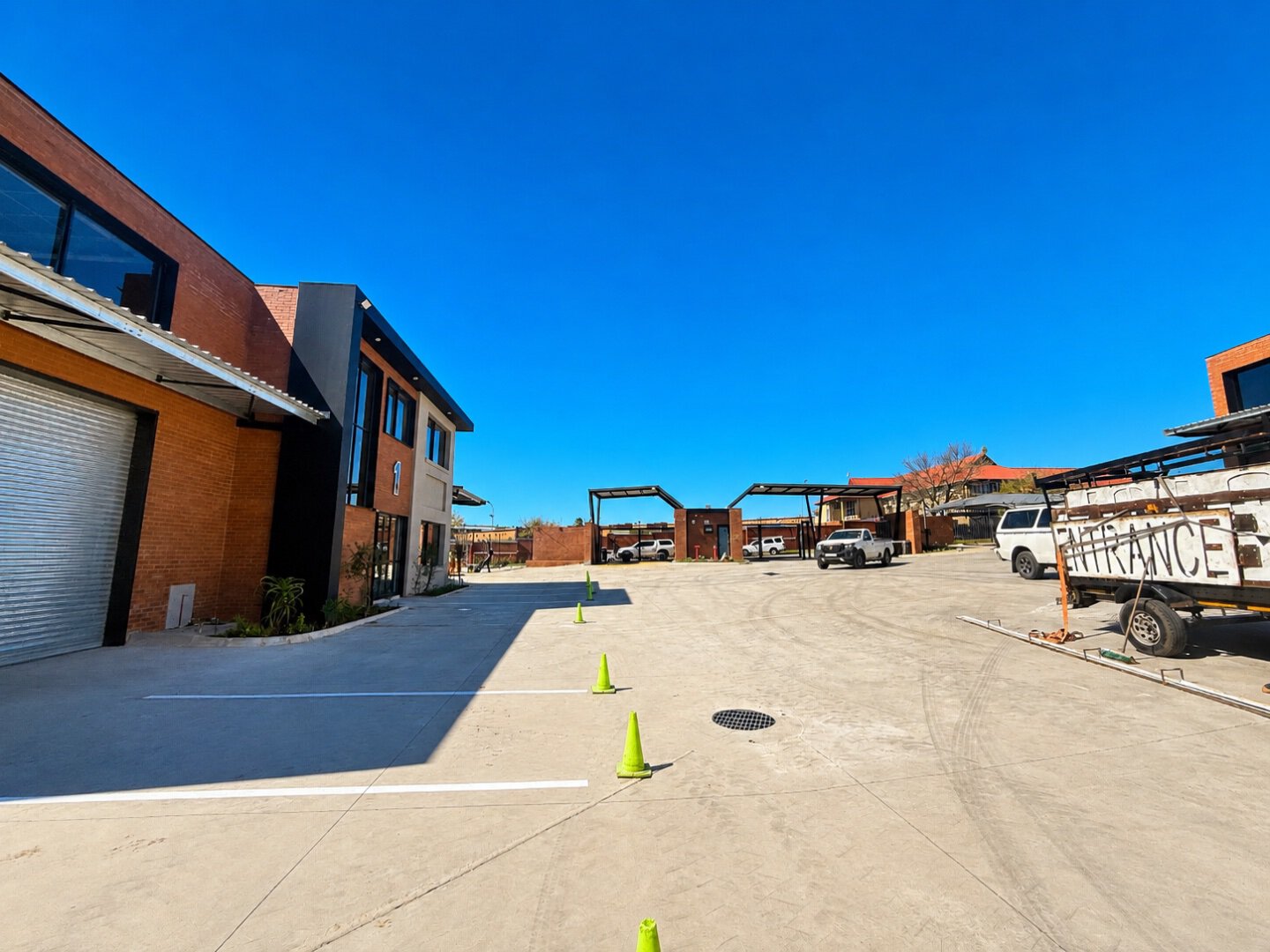 Industrial office and warehouse facility with parking lot, featuring modern brick and metal structures, under a bright blue sky with minimal clouds.