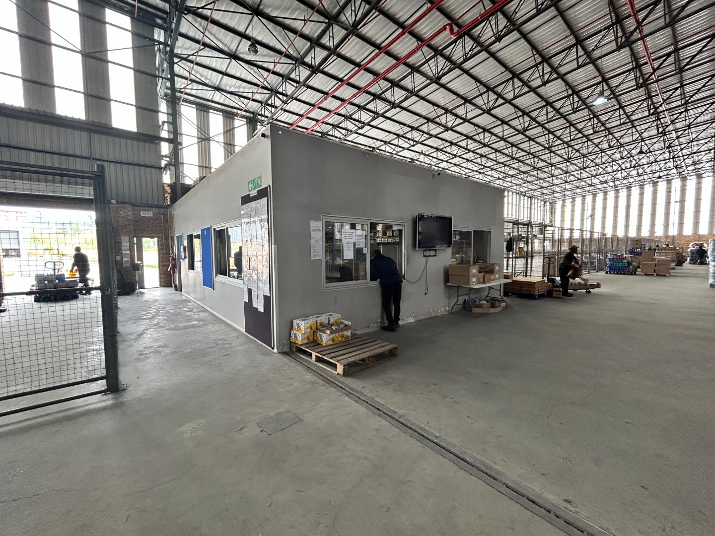 Currie Group Office and Warehouse Facility Modern office and warehouse space within a large industrial building, featuring a small office unit with a person working on a computer, surrounded by warehouse equipment and materials.