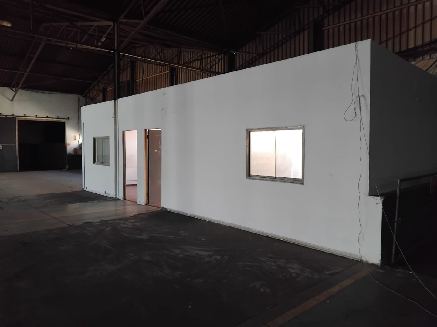 Office and warehouse interior under construction at Currie Group, showcasing a white partitioned wall with windows and door openings inside a large industrial building.