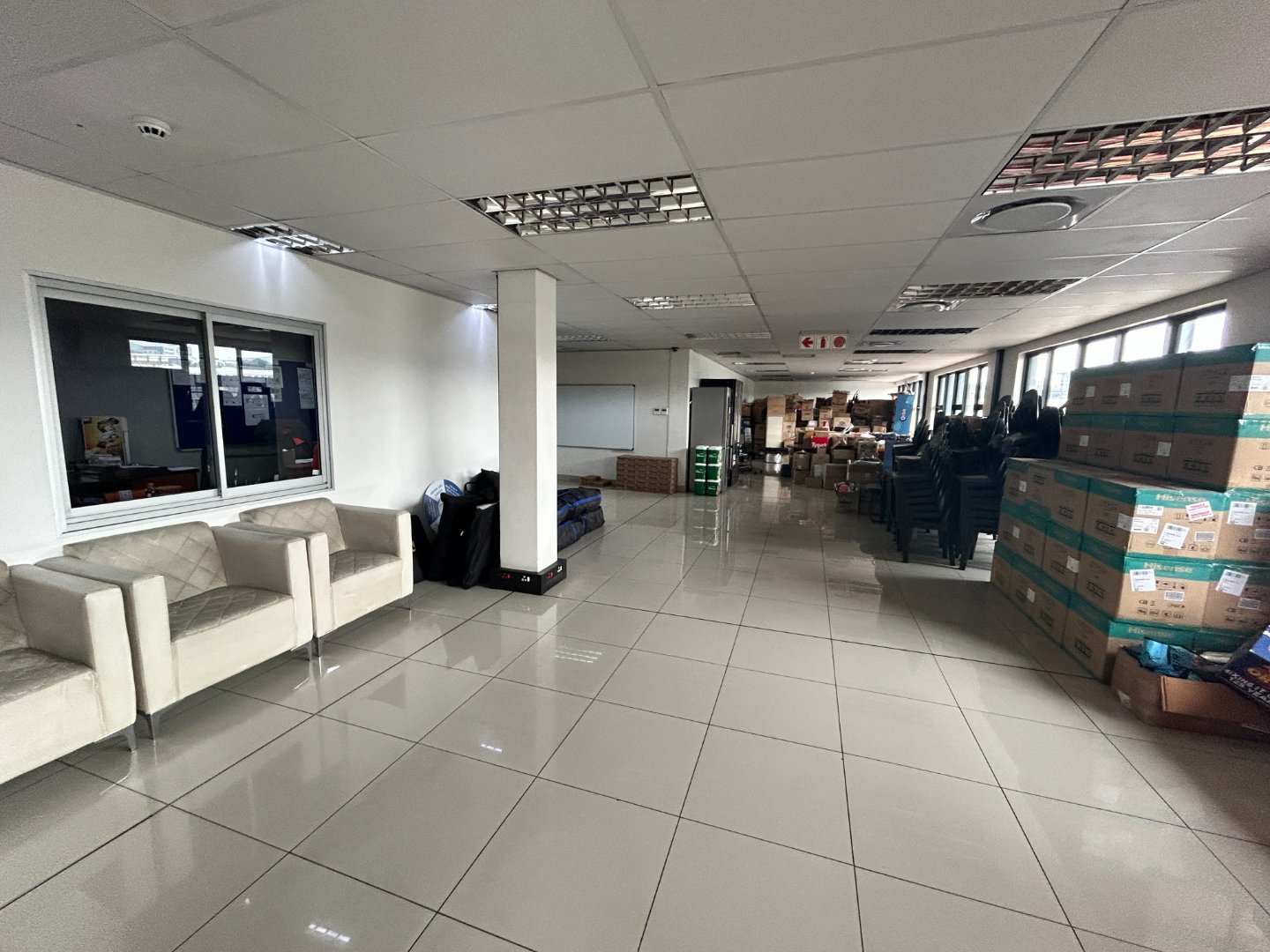 Office lobby with seating and stacked boxes at Currie Group warehouse. Modern office interior featuring white sofas, large windows, and a spacious layout with stacked boxes and office supplies.