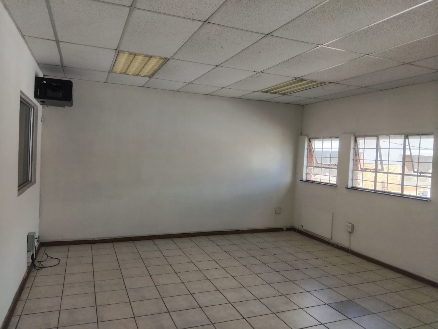 Modern Office Space with Large Windows and Tiled Floor Spacious office room featuring large windows that allow natural light, tiled flooring, and a simple ceiling with fluorescent lighting, ideal for business operations.