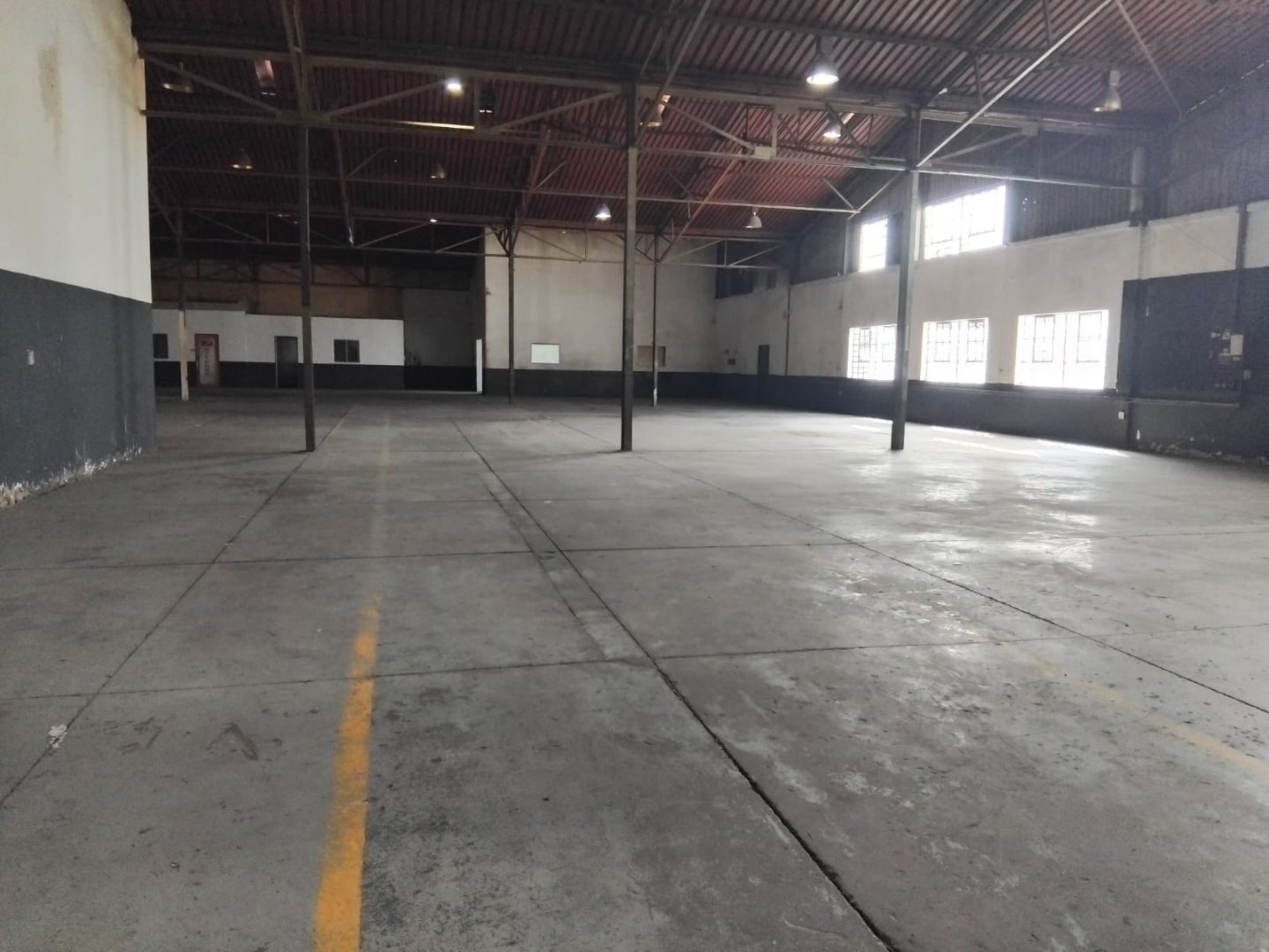Spacious Warehouse Interior An empty industrial warehouse with high ceilings, large windows, and concrete floors, showcasing a versatile space suitable for storage, manufacturing, or distribution operations.