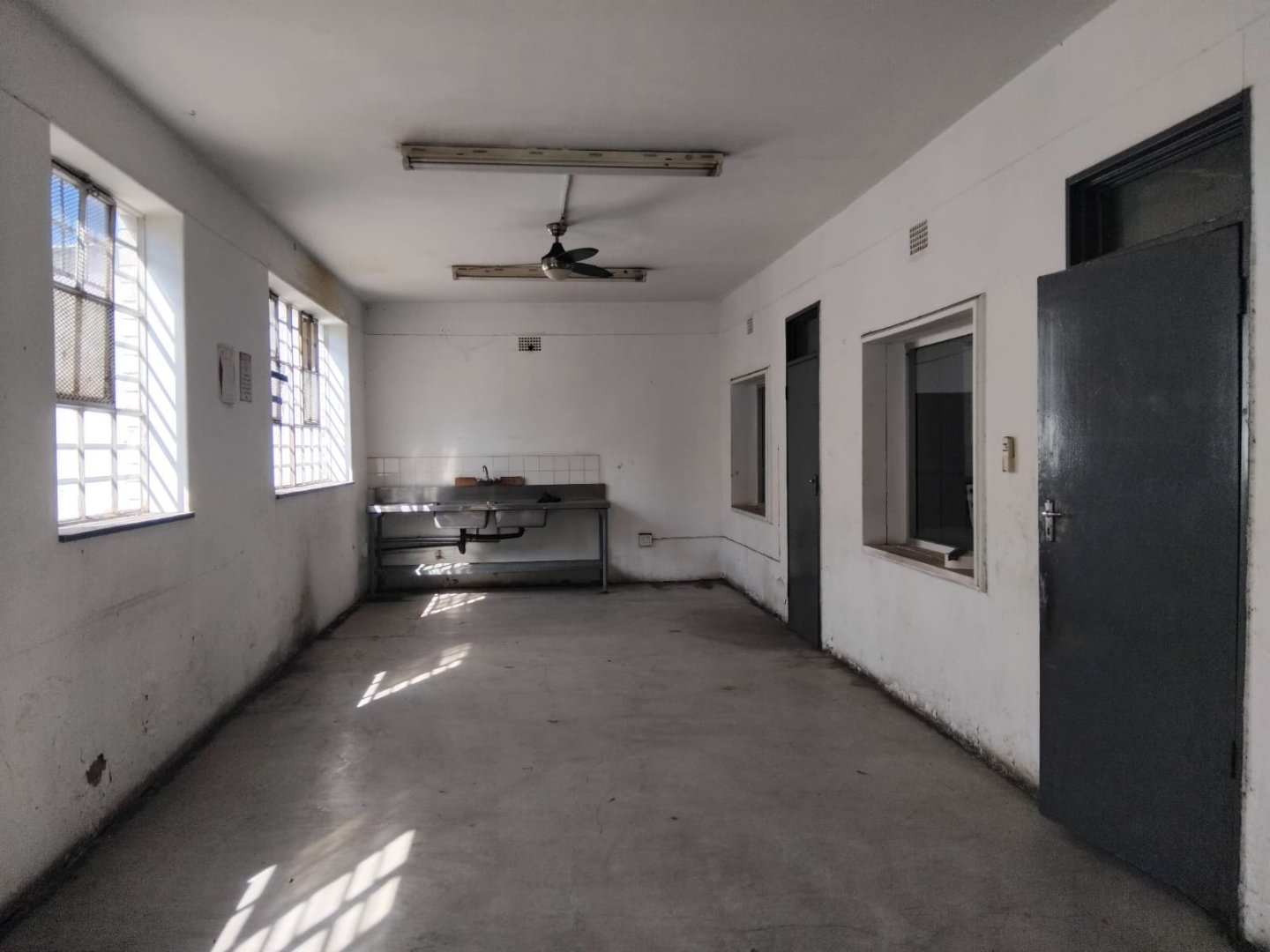 Industrial Office Space with Windows and Ceiling Fan Spacious industrial office area featuring large windows, a ceiling fan, and minimal furnishings, ideal for workspace or storage needs.