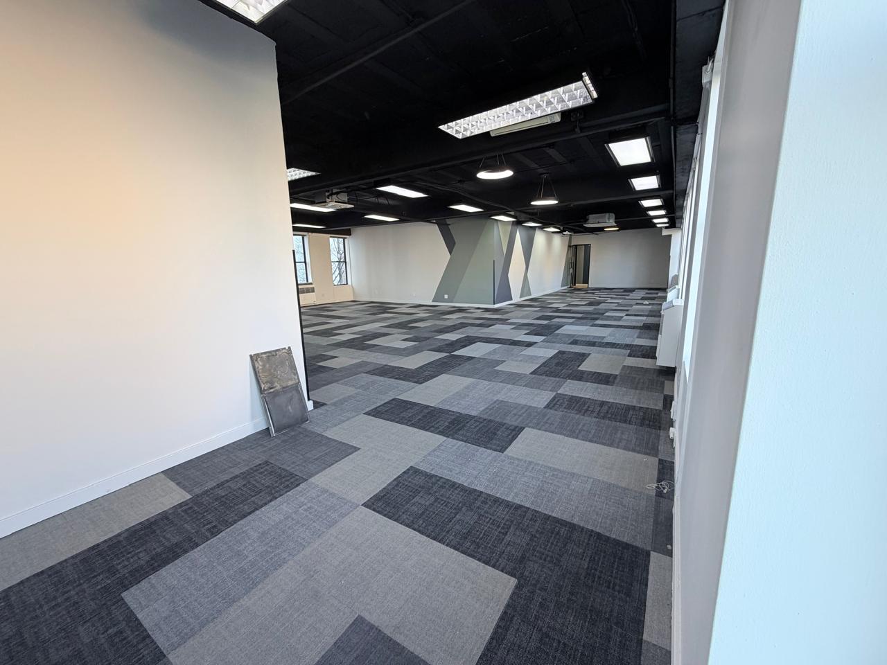 Modern office interior with spacious layout and contemporary design elements. Bright, open-plan office space featuring large windows, stylish carpeting, and sleek ceiling lighting.
