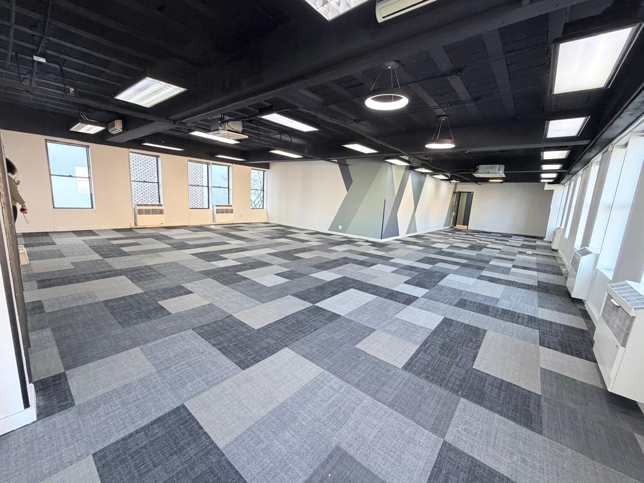 Modern office space with stylish carpet flooring and large windows A spacious, contemporary office interior featuring patterned carpet tiles, ample natural light from large windows, and a sleek ceiling design with modern lighting fixtures.