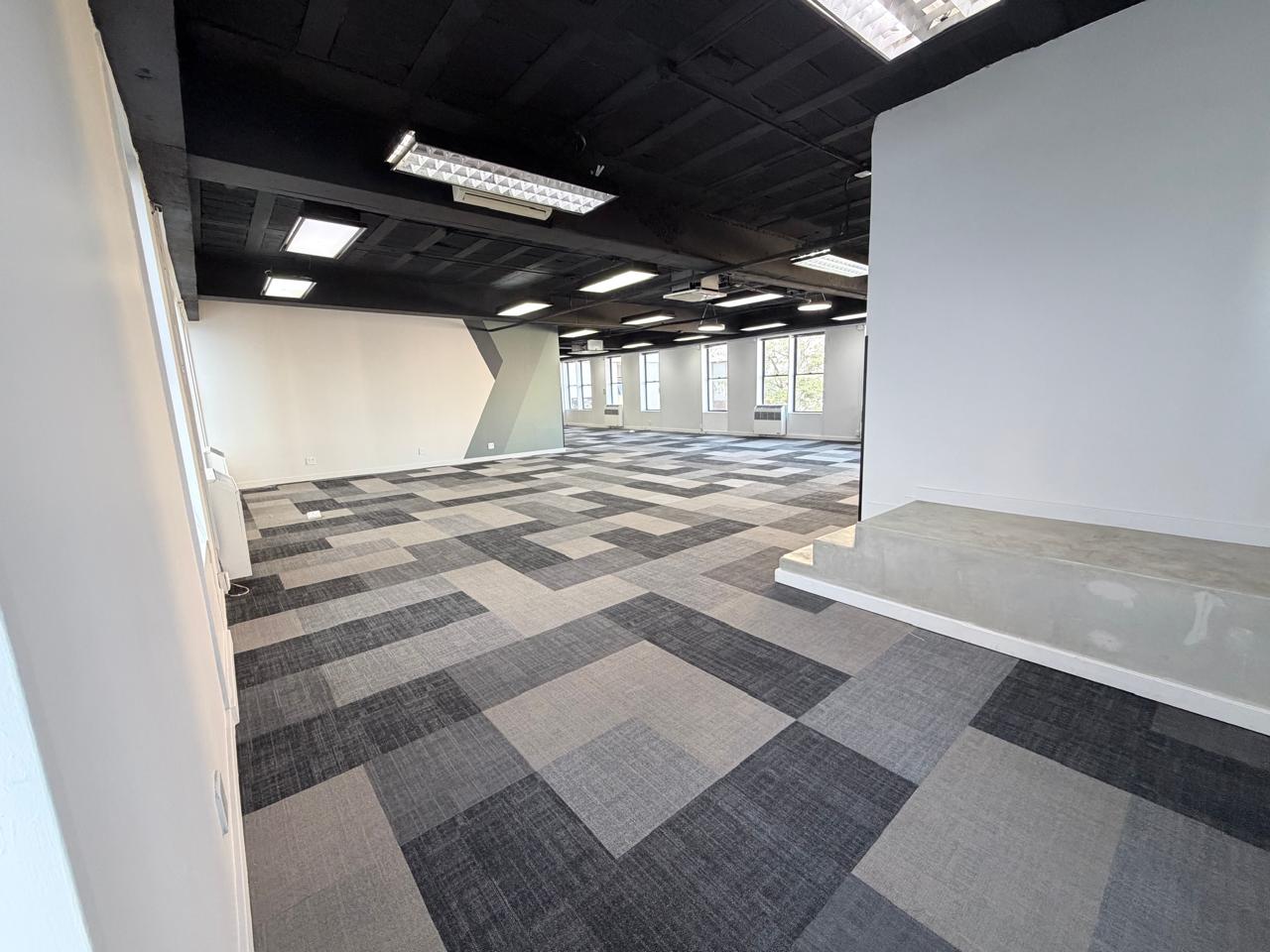 Modern office space with large windows and patterned carpet flooring. Office space with large windows and contemporary carpet tiles, providing a bright and professional environment suitable for various business needs.