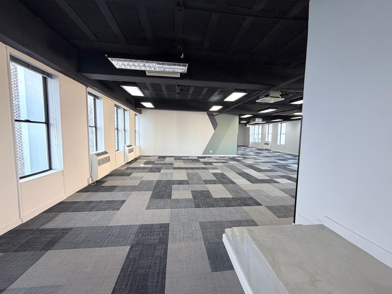 Modern office space with large windows and patterned carpet flooring. Office space with large windows and contemporary carpet tiles, providing a bright and professional environment suitable for various business activities.