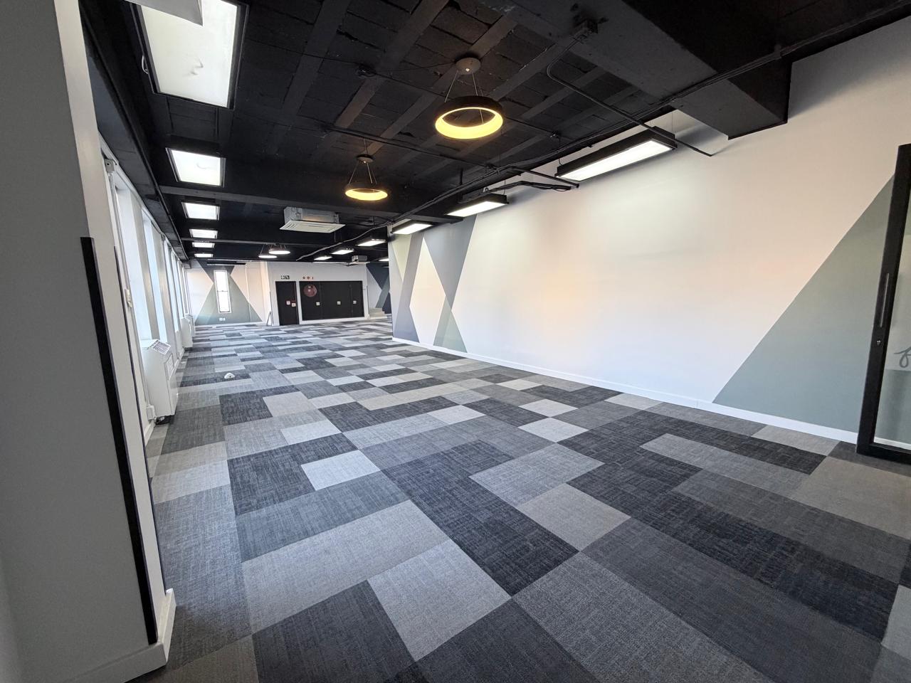 Modern Office Space with Geometric Wall Design Modern office interior featuring a spacious, well-lit room with geometric wall patterns and contemporary lighting fixtures. The space is ideal for meetings, collaborative work, or training sessions.