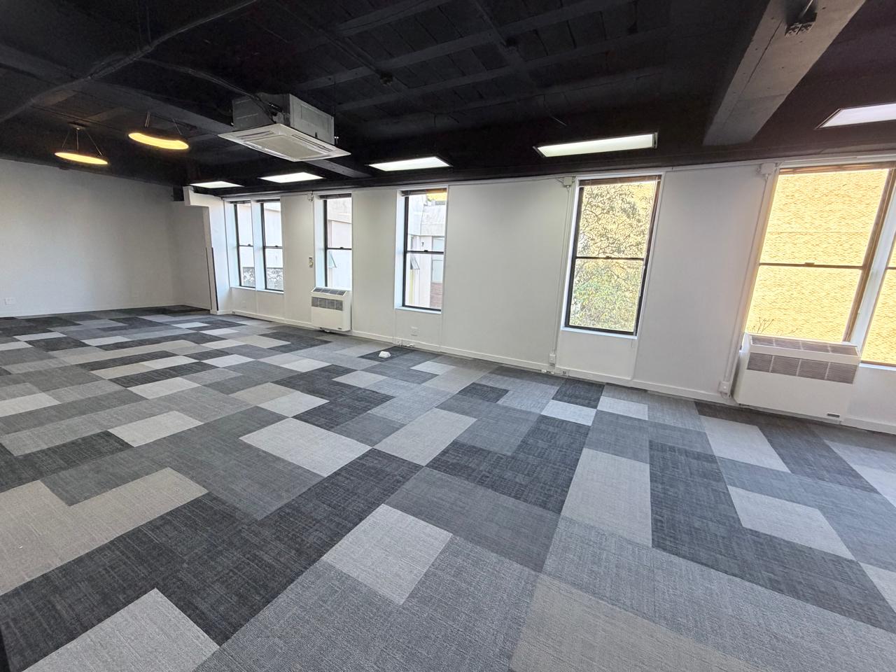 Modern Office Interior with Large Windows and Carpeted Floor Spacious office room featuring large windows, natural light, and a patterned carpeted floor, ideal for a professional workspace.
