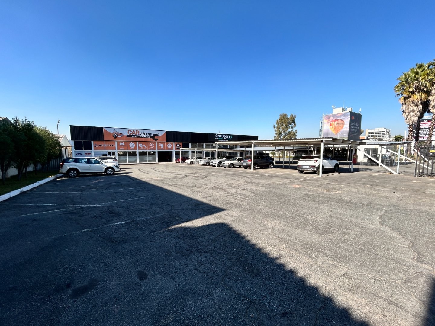 Spacious car dealership with multiple vehicles parked in front, modern building, clear blue sky, and surrounding trees in Randburg.