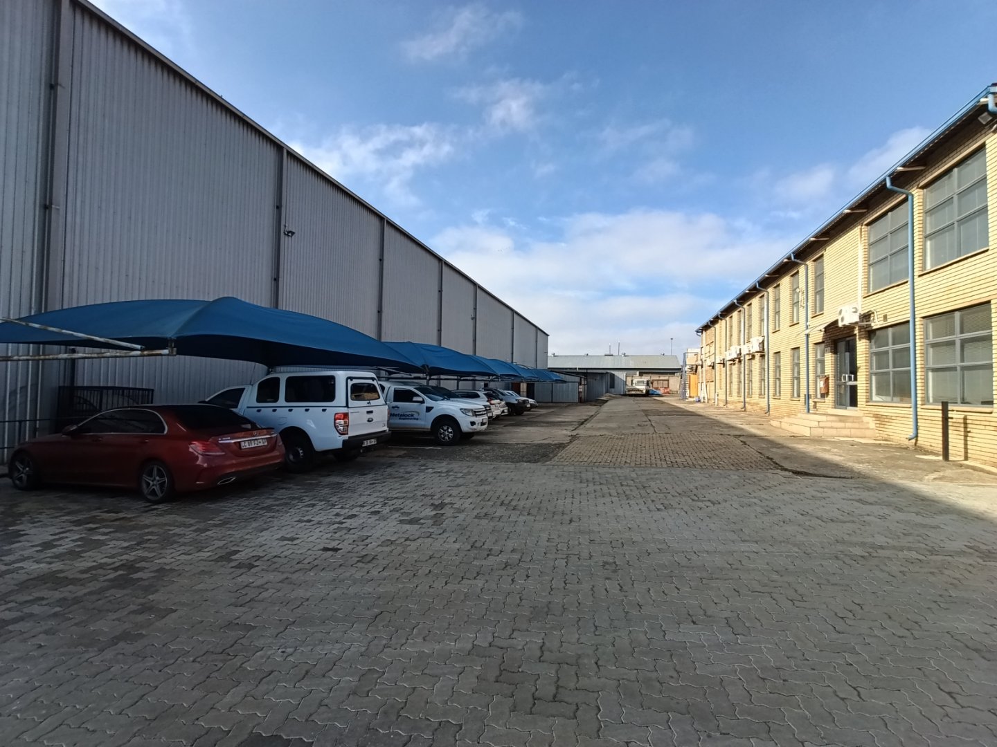 Exterior view of Currie Group offices and warehouses with parked cars and blue awnings under a partly cloudy sky.