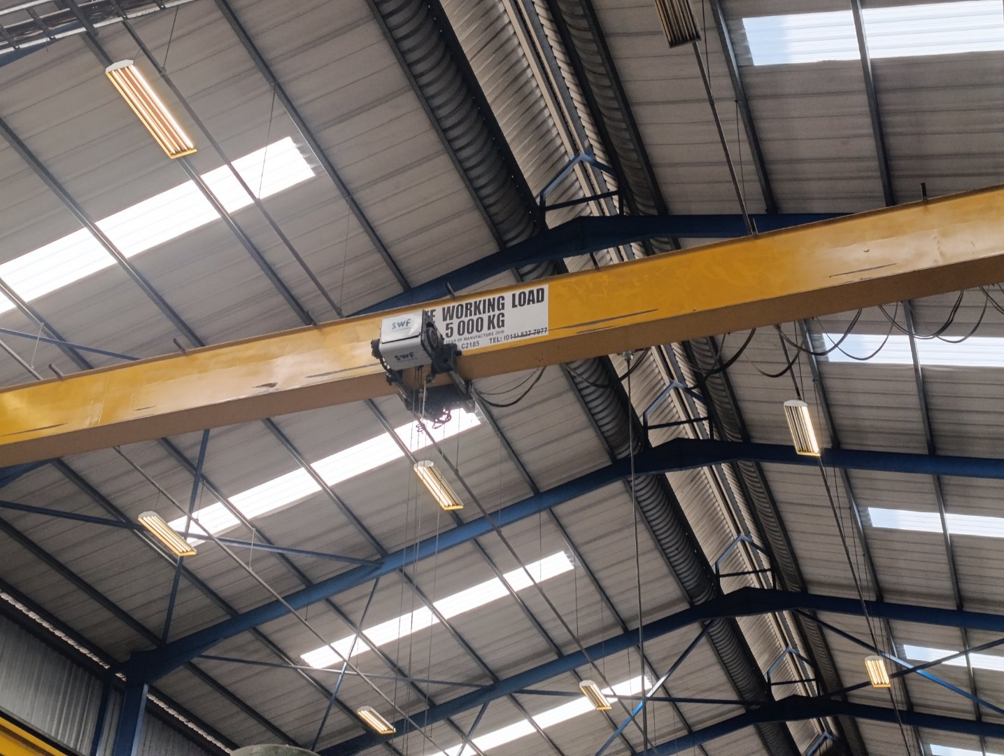 Industrial Warehouse Overhead Crane Heavy-duty overhead crane in a modern industrial warehouse with high ceilings and skylights, used for lifting and moving heavy loads.