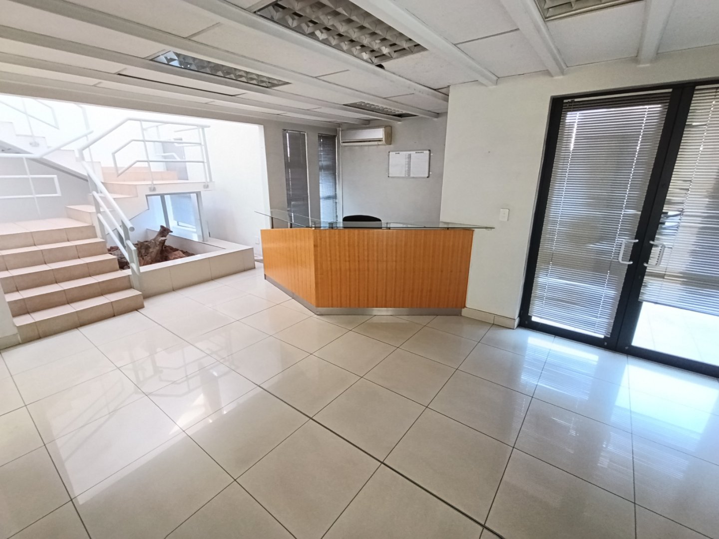 Currie Group Office Reception Area Modern office reception area with tiled flooring, a wooden reception desk, large windows, and a staircase leading to upper floors.