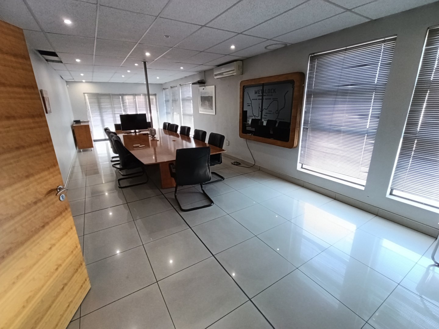 Currie Group Office Meeting Room Modern office meeting room with a large wooden table, black chairs, and large windows with blinds, bright and professional environment.