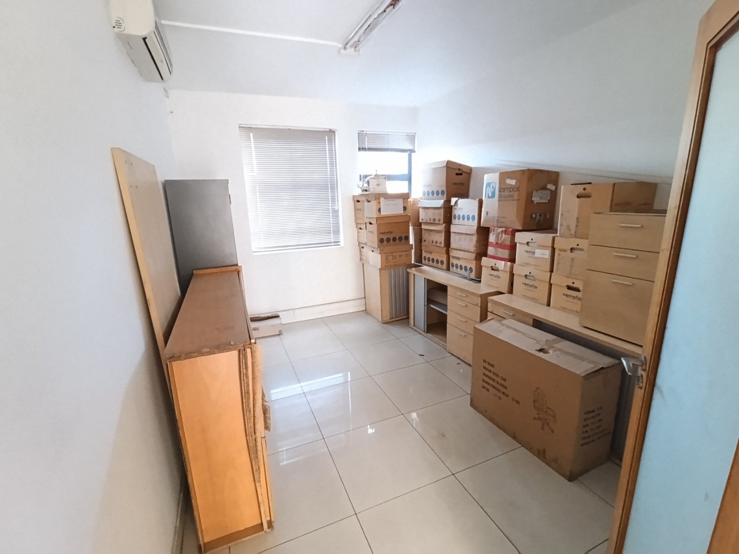 Warehouse Storage Area at Currie Group Interior view of a warehouse with stacked boxes and storage furniture, bright natural light from windows, and a clean tiled floor.