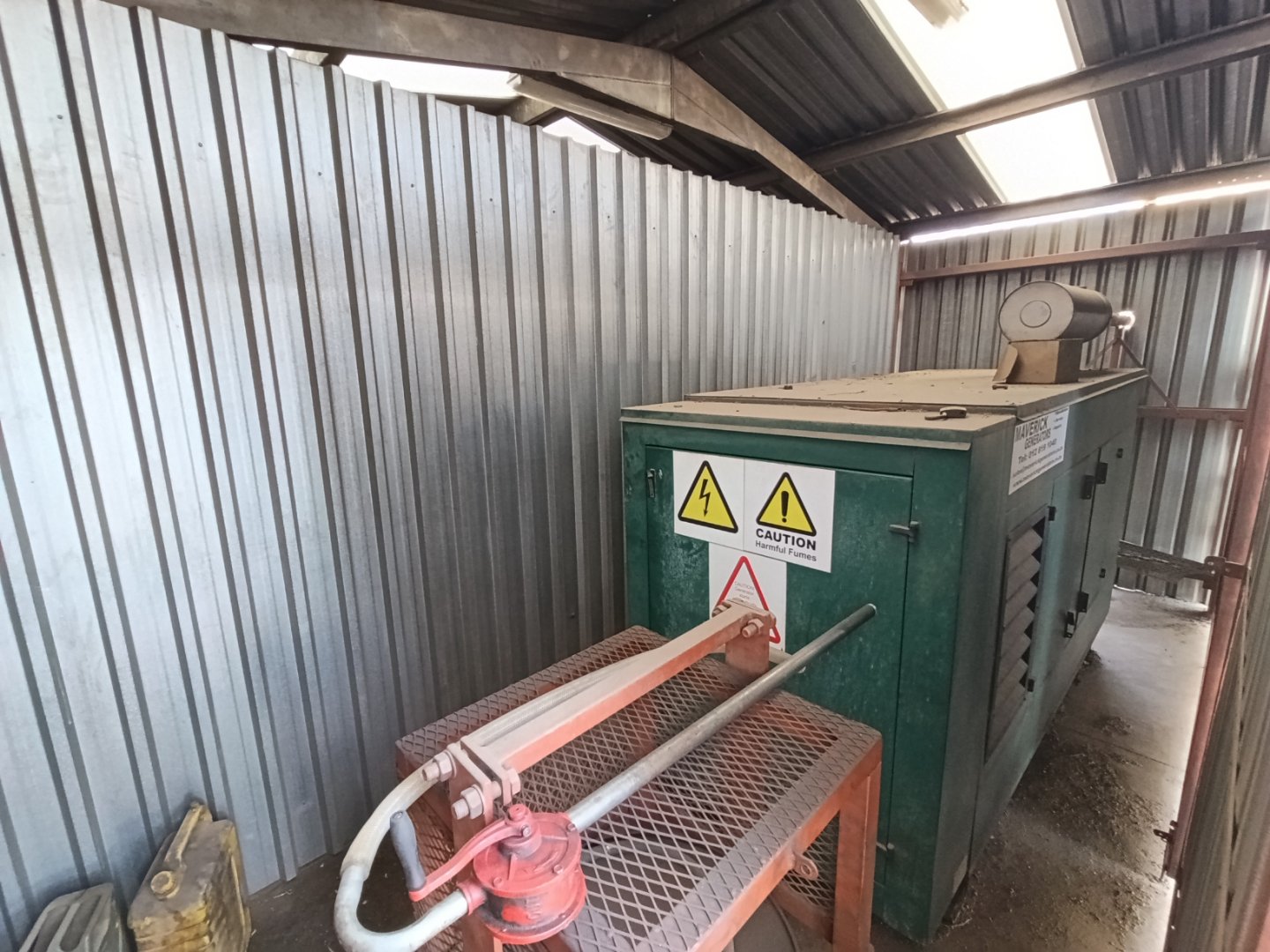 Industrial Electrical Equipment in Warehouse Industrial electrical equipment inside a warehouse with metal walls and a roof, featuring a large green electrical box and a smaller red component.