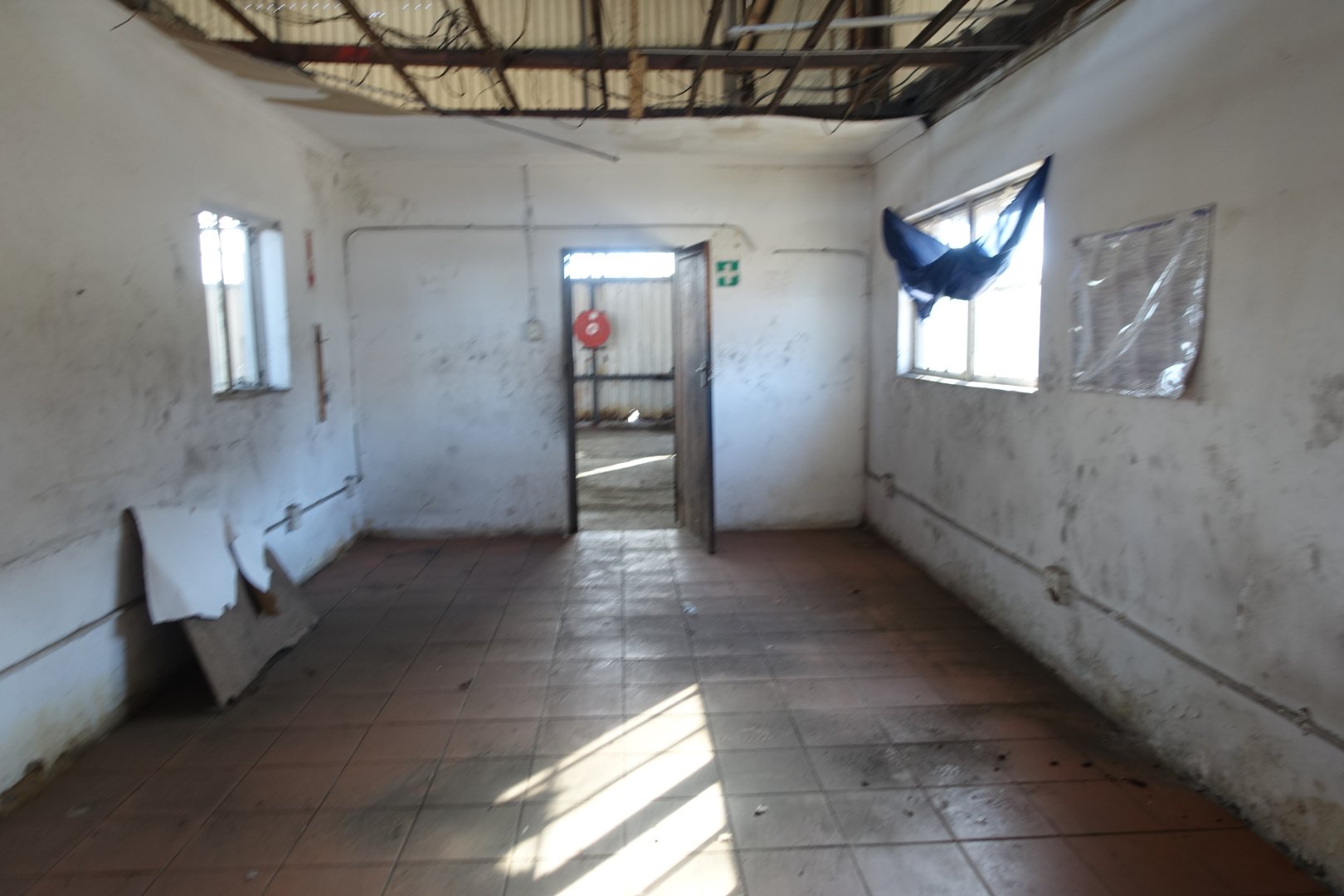 Old Warehouse Interior at Currie Group Interior of an old warehouse with worn walls, broken windows, and a partially damaged ceiling, showcasing the building's age and industrial character.