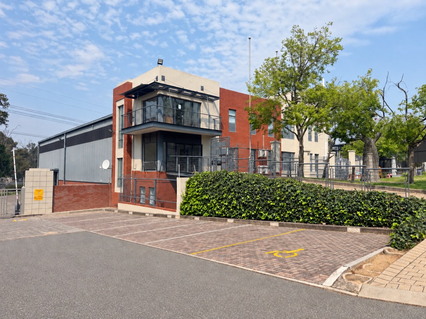 Contemporary office building with glass windows and brick facade in Bryanston, featuring parking spaces and surrounding greenery.