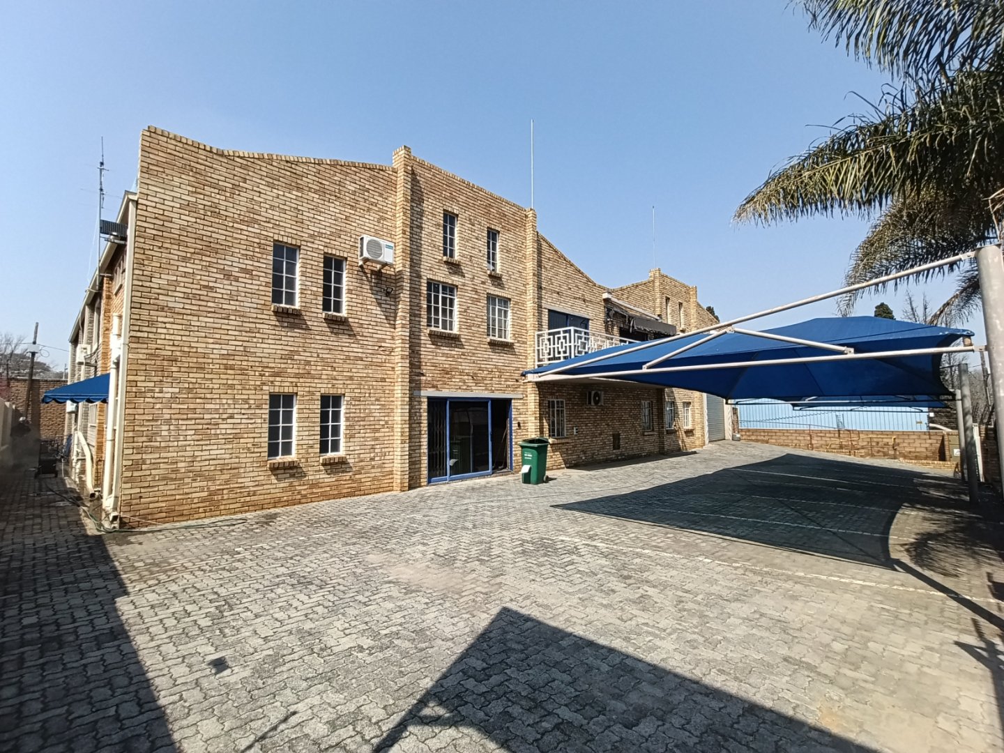Exterior view of Currie Group offices and warehouses with brick facade, outdoor seating, and palm trees, showcasing a professional industrial facility since 1887.