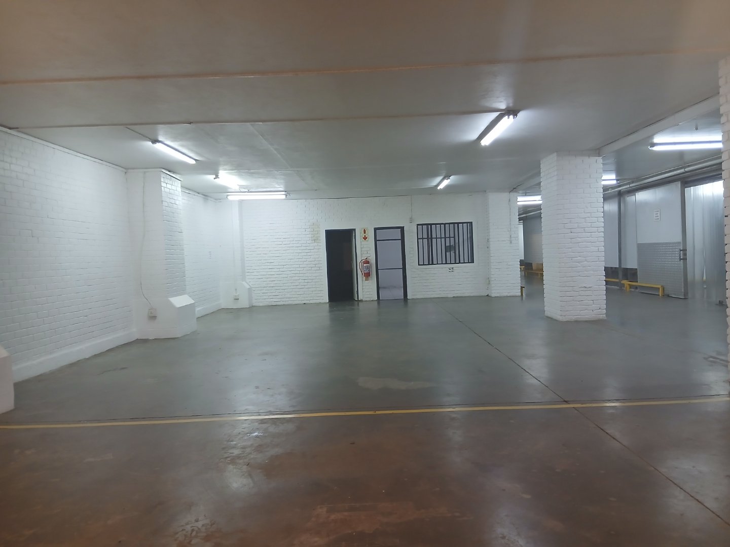 Spacious Warehouse Interior at Currie Group Interior view of a large, empty warehouse with white brick walls, concrete floors, and bright overhead lighting at Currie Group offices and warehouses.