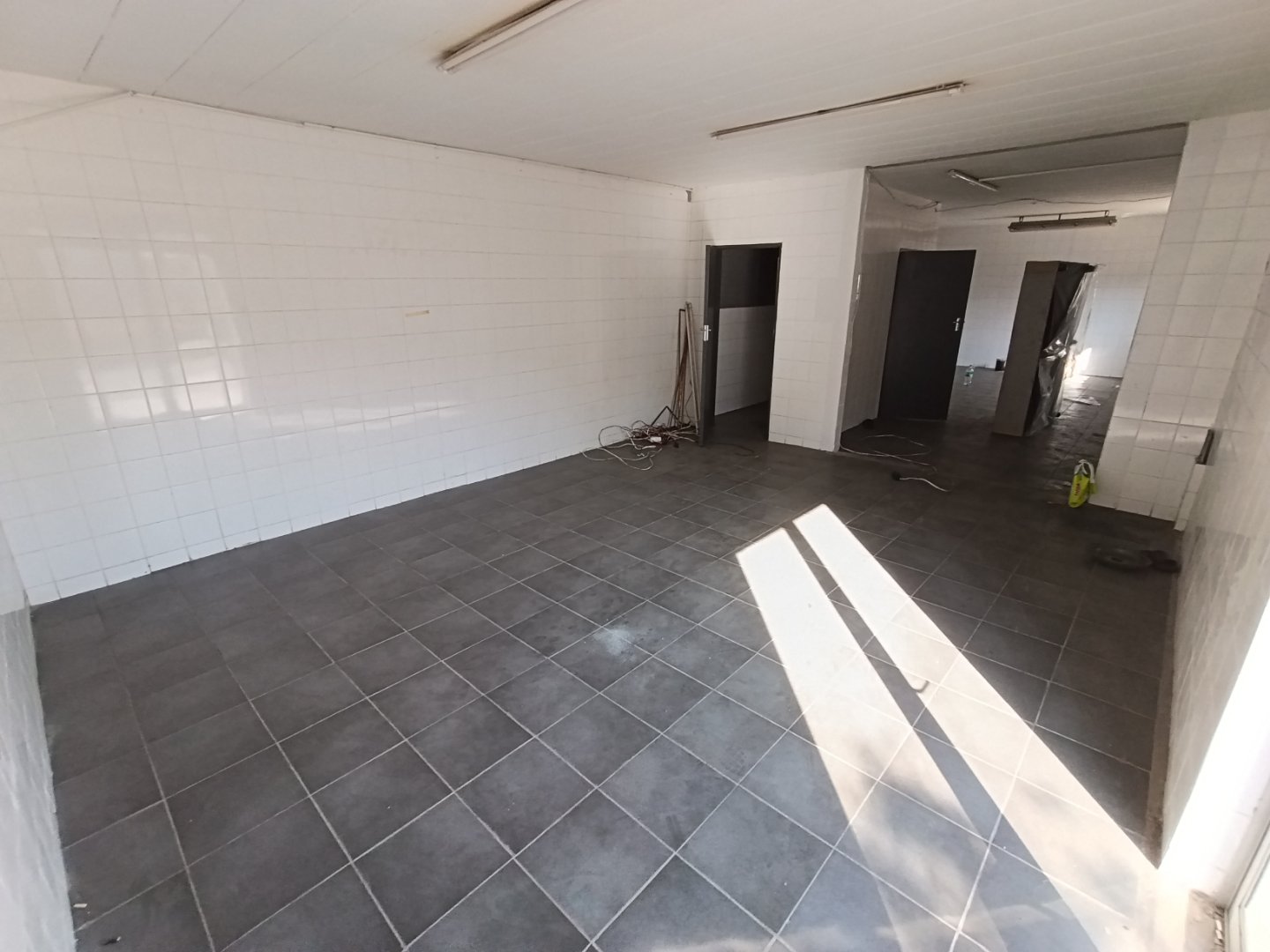 Industrial Warehouse Interior Renovation Empty industrial warehouse with tiled floors and white tiled walls, under renovation, with sunlight streaming in.