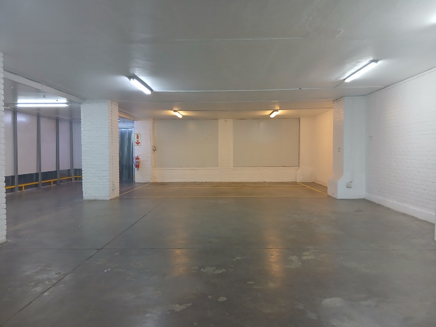Underground Parking Garage Space Spacious underground parking garage with white brick walls, concrete floor, and overhead lighting, suitable for vehicles and storage.