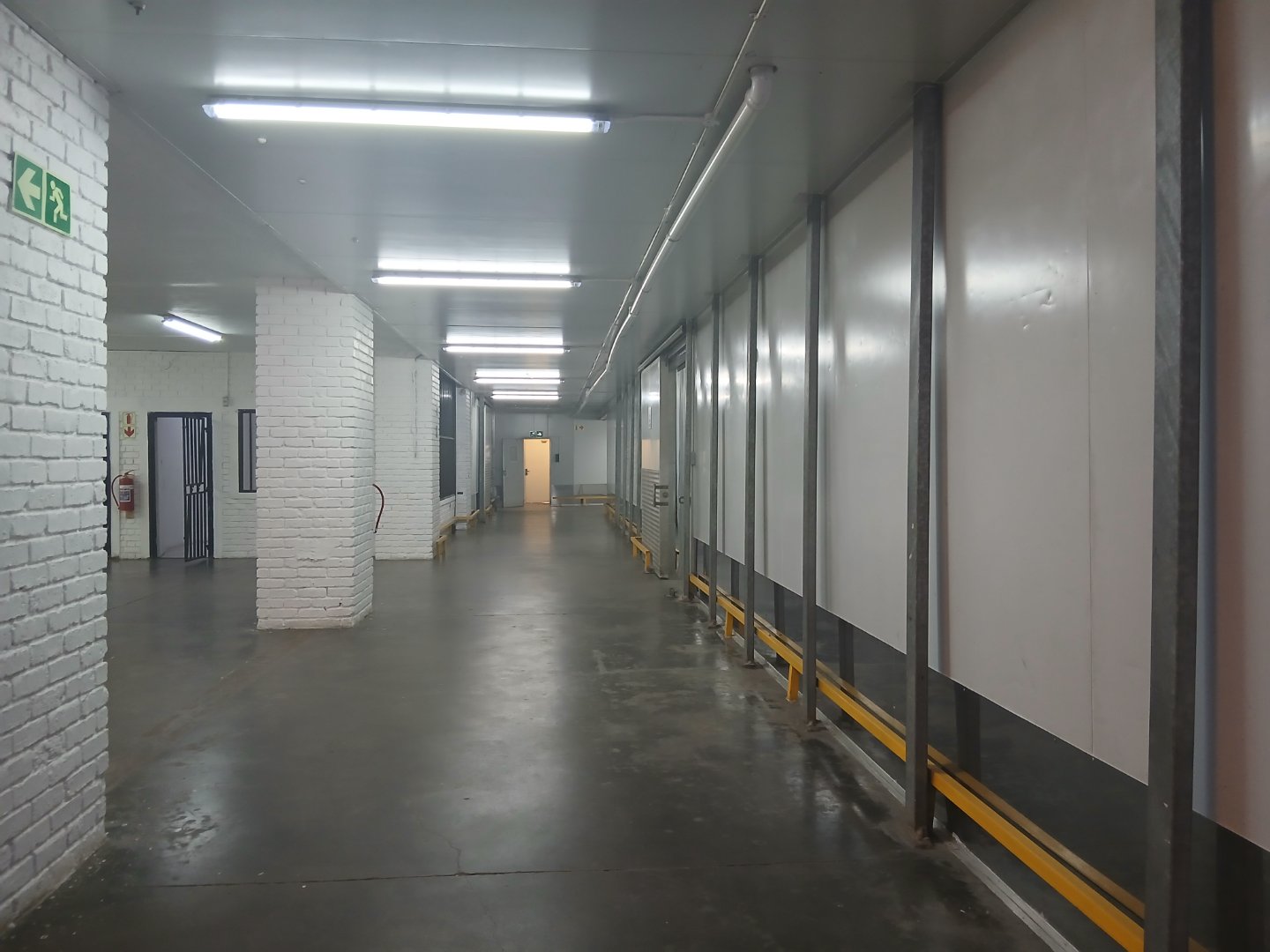 Industrial Warehouse Interior Spacious industrial warehouse with white brick walls, concrete floor, and overhead lighting, featuring a loading dock area with safety barriers.