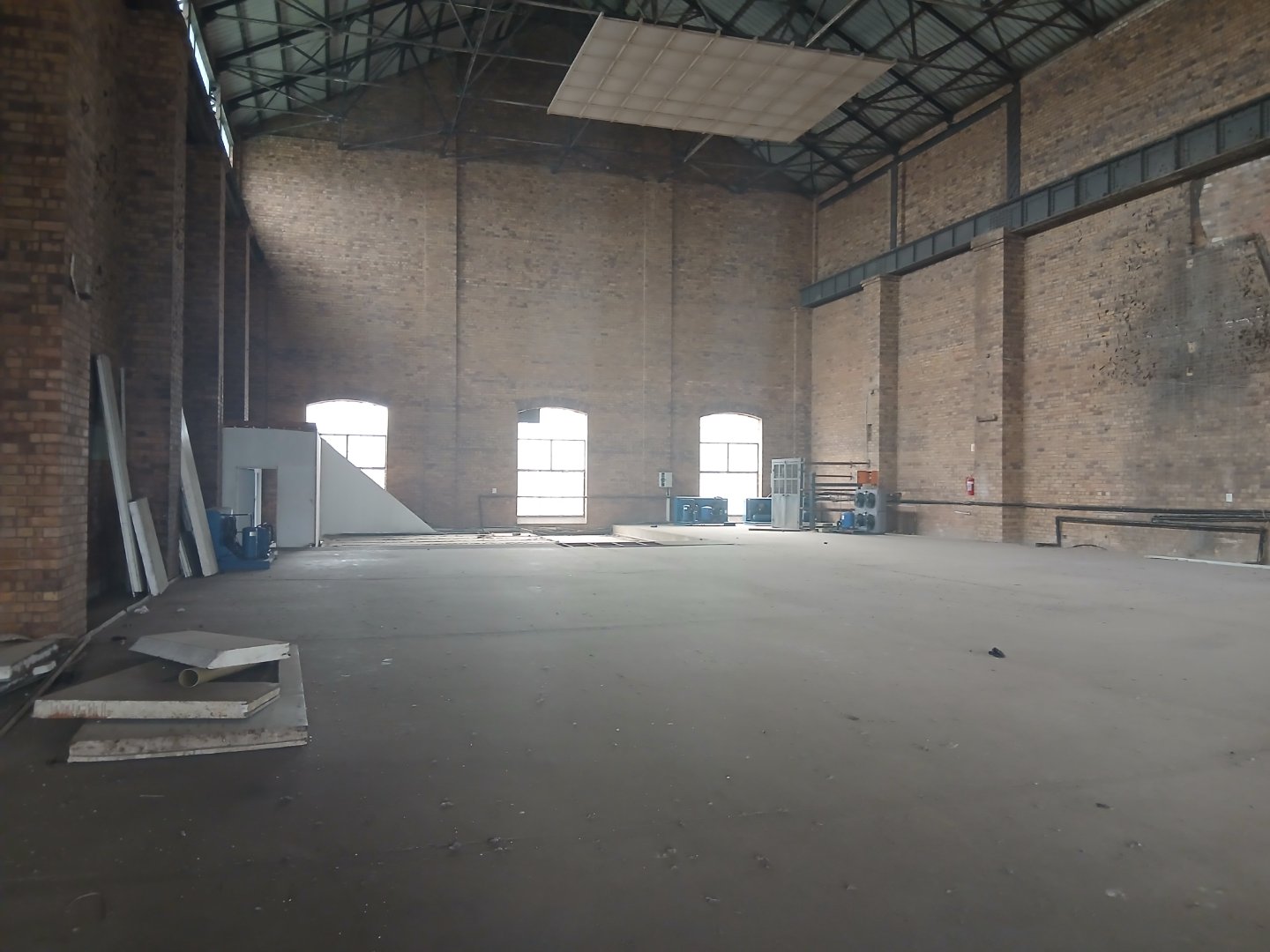Spacious industrial warehouse interior Large empty warehouse with high ceilings, brick walls, and natural light from windows, suitable for storage or manufacturing.
