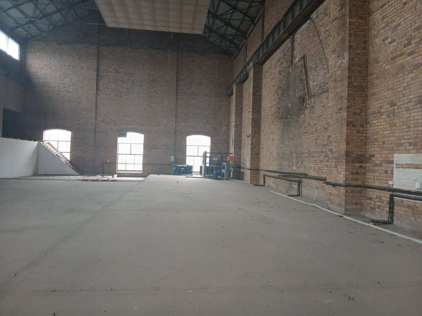 Spacious industrial warehouse interior Large empty warehouse with brick walls and high ceilings, suitable for storage or manufacturing, with natural light coming through windows.