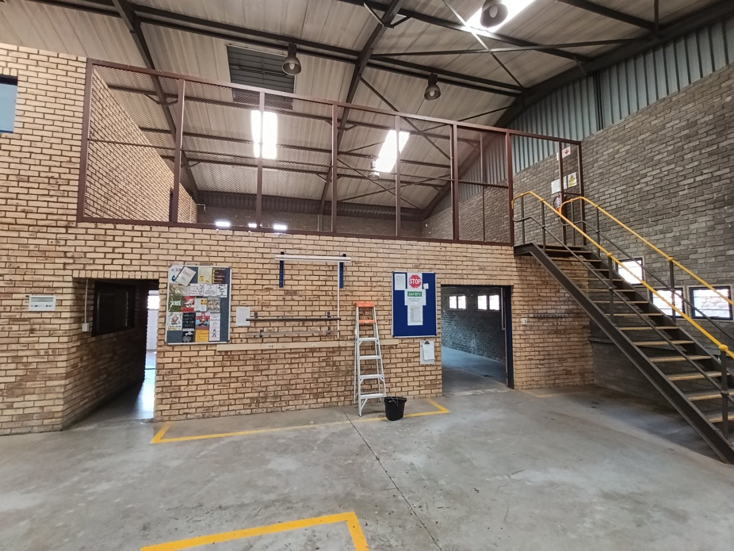 Industrial Office Space at Currie Group Spacious industrial office area with brick walls, staircase, and mezzanine level, suitable for warehousing and office use at Currie Group.