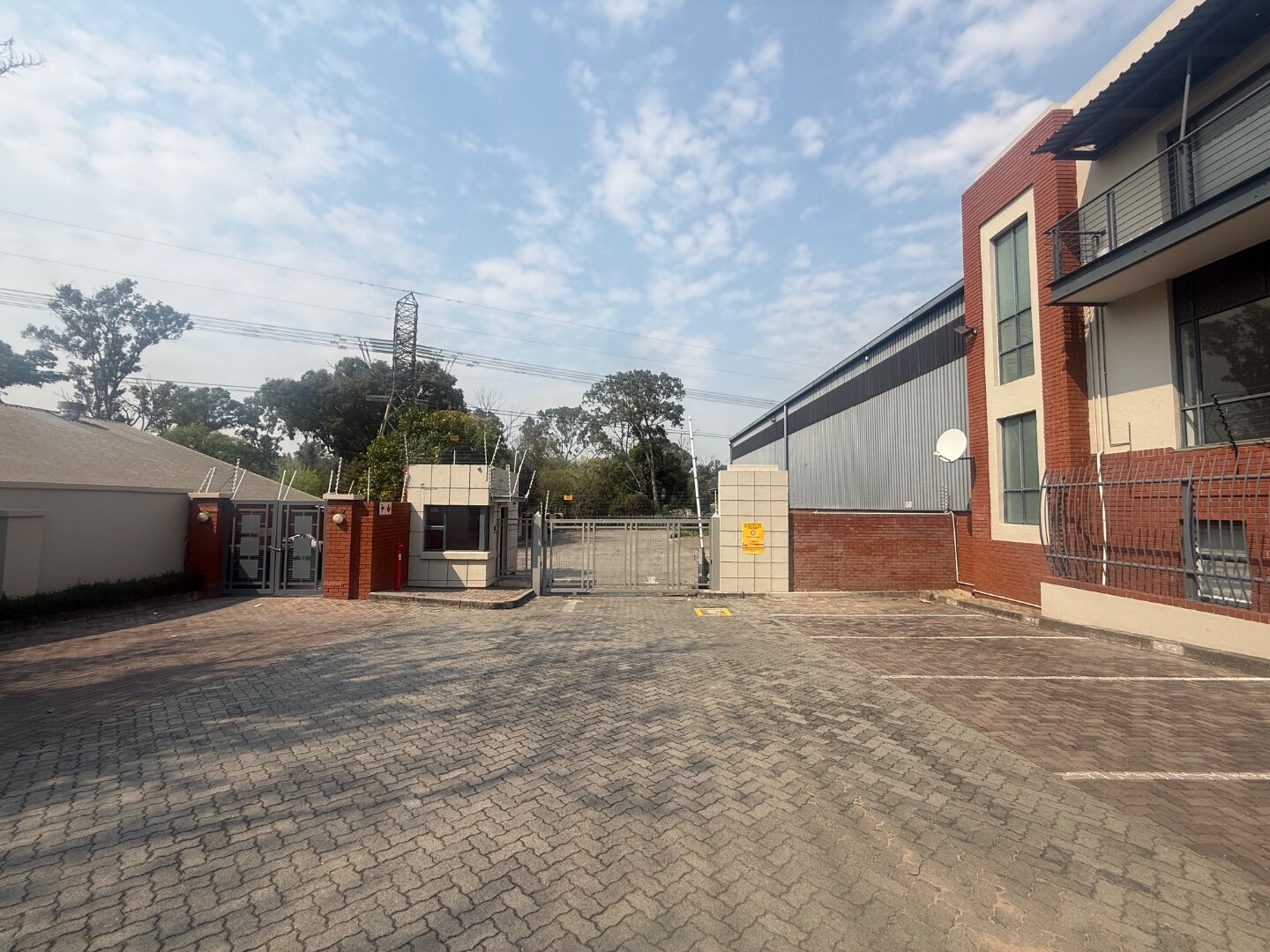 Spacious parking lot in front of modern commercial building with secure gated entrance and surrounding trees.