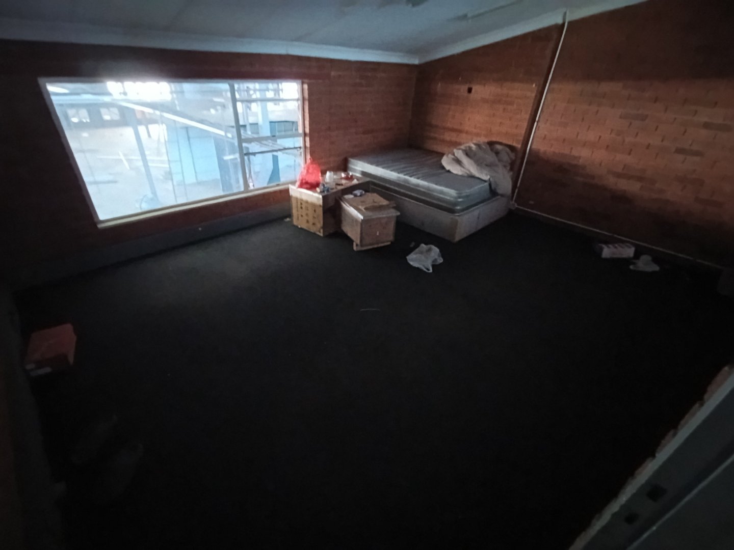 Industrial Warehouse Interior in Alrode Empty industrial warehouse space in Alrode with a mattress and scattered items, featuring large windows and brick walls.
