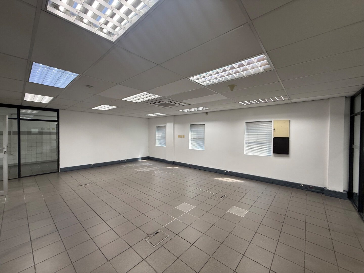 Spacious Commercial Warehouse Interior Bright, empty commercial warehouse with tiled flooring, white walls, and ceiling lights, suitable for storage or office space.