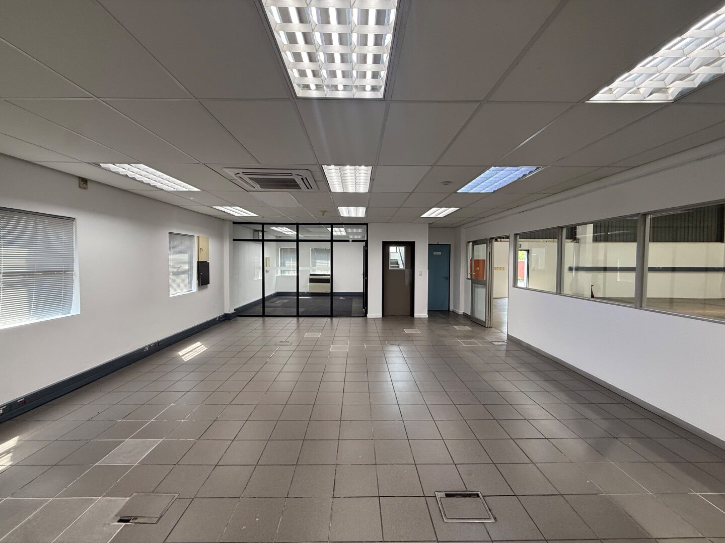 Spacious Commercial Warehouse Interior Bright, empty commercial warehouse interior with tiled flooring, large windows, and ceiling lights, suitable for office or storage use.