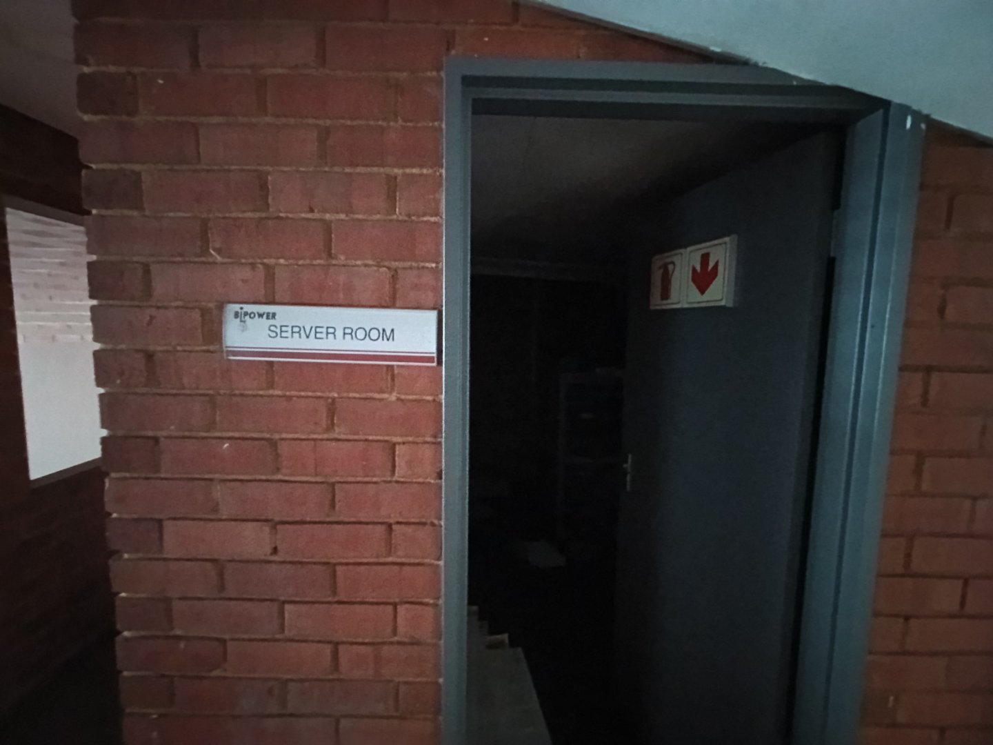 Server Room in Industrial Warehouse Industrial warehouse interior showing a server room entrance with a sign, brick walls, and a partially open door.