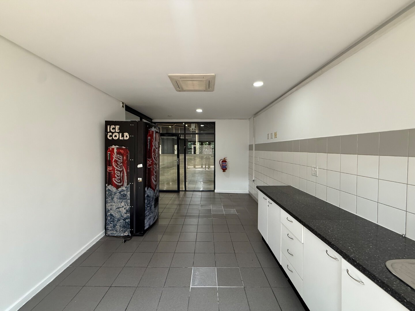 Modern Commercial Warehouse Interior Spacious commercial warehouse interior with vending machines and a long countertop, featuring clean white walls and tiled flooring, suitable for storage or office use.