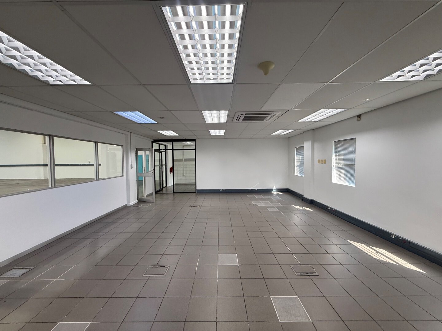 Spacious Commercial Warehouse Interior Bright, empty commercial warehouse with tiled flooring, white walls, and ceiling lights, suitable for storage or industrial use.