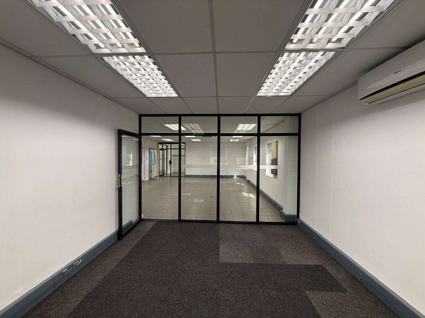 Modern Office Space with Glass Partitions Spacious modern office interior with glass partitions, white walls, and ceiling lights, suitable for corporate use.