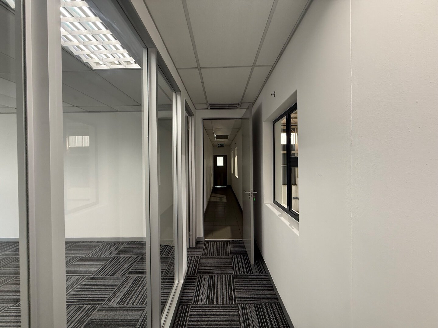 Modern Office Corridor with Glass Partitions Spacious office corridor with glass partitions and natural light, leading to private offices and meeting rooms in a professional commercial building.