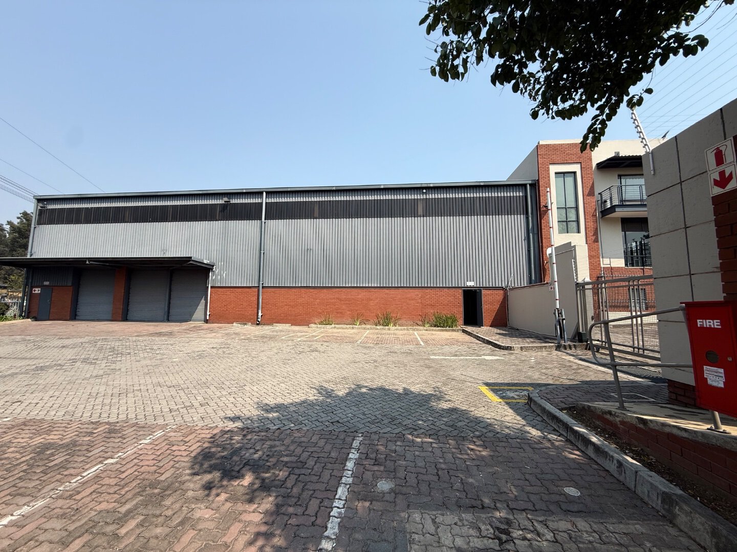 Large modern warehouse with brick and metal exterior in Bryanston, South Africa, with parking lot and fire safety equipment visible.