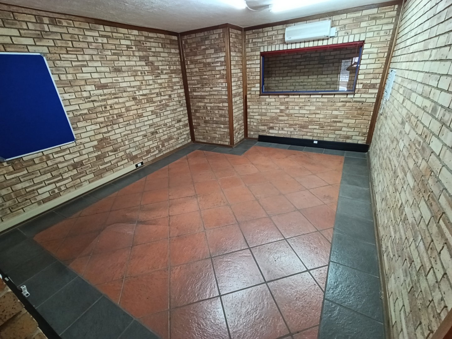 Empty office room with brick walls, tiled floor, and a window, showcasing a professional workspace environment.