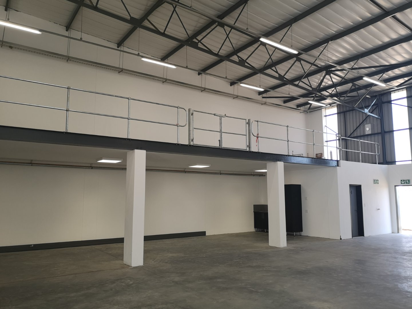 Spacious industrial warehouse with mezzanine level, high ceilings, and large windows for natural light, showcasing modern office and storage space.