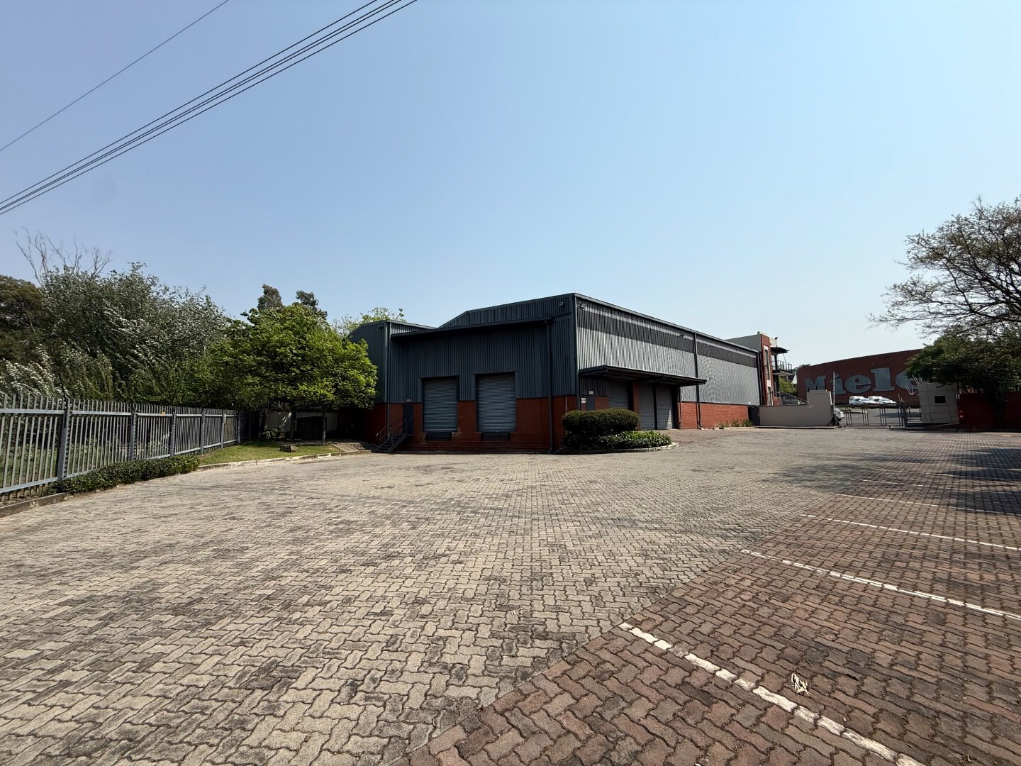 Commercial Warehouse in Bryanston Modern commercial warehouse building in Bryanston with ample parking space and surrounding greenery, suitable for industrial and logistics purposes.