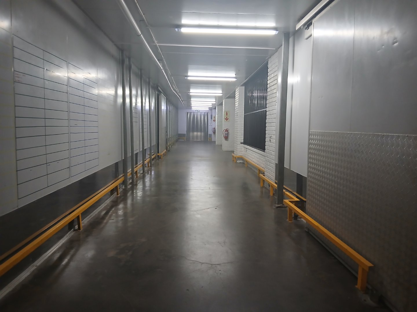 Industrial Warehouse Corridor Spacious industrial warehouse corridor with metal walls, bright lighting, and safety barriers along the sides.
